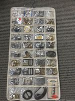 White hanging organizer with clear pockets containing numerous metal buckles and loops in silver, gold, and bronze tones