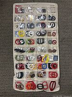 Front view of the first white hanging organizer with divided clear pockets displaying many multicolored fashion belt loops and slides of different shapes and sizes, arranged in rows.
