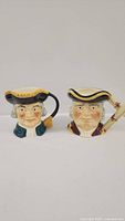 Front view of two collectible ceramic mugs depicting 18th-century characters in tricorne hats.