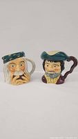 Two Royal Doulton collectible mugs of character designs, side by side on a flat surface.