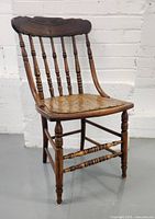 Side view of antique pressback spindle chair showing contoured seat, turned legs and spindles, and carved top rail.