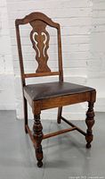 Full view of antique wood chair angled to show side, backrest carving, turned legs and leather seat