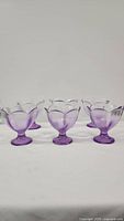 Front row view of six purple glass dessert scoop cups with scalloped rims on a white background.