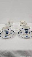 Front view of all five teacups and saucers showing two blue and white Holland sets and three other teacups including white Fire King and Japan delicate patterned sets.