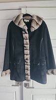 Full front view of the Jessica black coat with faux fur trim hanging on hanger showing button closure, two front pockets, and the overall coat design and length.