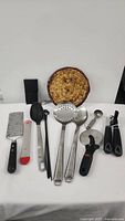 Full view of the utensils laid out showing the spoons, pizza cutter, graters, and other tools