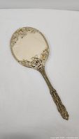 Full view of the antique hand mirror with ornate metal frame showing rose floral details and handle