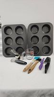 Full view of entire lot including two large muffin baking trays, Pyrex measuring cup, stainless steel measuring cups, various kitchen utensils and knives.