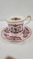 Side view of Royal Albert Blue & Gold teacup and saucer showing pink background, floral and gold decoration, gold handle