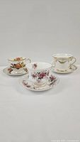 Photo showing 3 different vintage teacups and saucers, each with distinct floral patterns and gold trim.