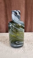 Tall glass decorative piece with black, green, and white swirling pattern against a brown backdrop on a lace tablecloth.