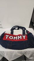 Front view of antique style Tommy Hilfiger duffel bag showing large red panel with stitched TOMMY letters on navy blue canvas.