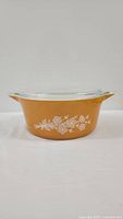 Side view of the golden yellow vintage Pyrex casserole dish with white butterfly floral pattern and handles on each side.