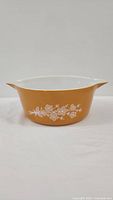 Side view of vintage Pyrex Butterfly Gold 475 round casserole dish with white floral pattern on gold ground and side handles