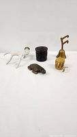 Photo of all four items including the black resin carved trinket box, wooden turtle, faux antler figurine, and brass mechanical sharpener arranged on a white background.