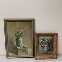 Two framed oil paintings of flower still lifes, one on a stool and one in a jug.