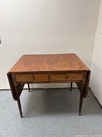 Front view of antique drop leaf table showing two drawers and drop leaves folded down.