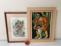 Photo showing two framed art lithographs side by side, with an apple for scale.