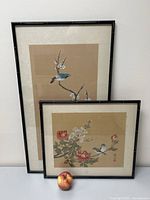 Two framed silk paintings side by side on table with apple for scale