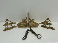 Front view showing two brass bookends, two handles, and decorative chain with crowns arranged on white surface