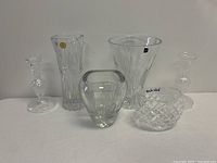 Photo of two clear crystal glass candle holders and four various clear crystal glass vases on a white surface