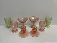 Front view of 2 green tumblers, 2 pink tumblers, 2 pink cocktail glasses, and 2 pink candle holders arranged on surface