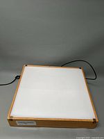 View of the Gagne Porta-Trace light box with wooden frame and white top surface, showing the full item unplugged on a gray surface.