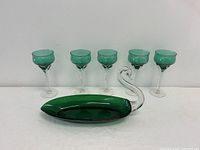 Five emerald green stemmed glasses and one large elongated candy dish with a clear twisted stem handle, displayed side by side on white background.