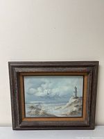 Full view of framed lighthouse coastal seascape painting against a light wall.