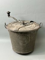 Full view of the metal Universal Bread Maker showing embossed logo and hand crank on lid.