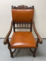 Front view showing full chair with carved wooden frame, brown leather seat and back, and studded trim details