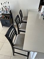 Three dark wood ladder-back barstools with light fabric cushions placed in front of a white kitchen counter. Cushions appear lightly stained.