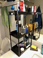 Front view of the black metal 3-tier bathroom organizer with various toiletries on each shelf.
