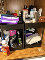 Two black plastic two-tier bathroom organizers filled with miscellaneous toiletries showing size and structure.