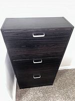 Front view of the closed black wood shoe rack with three drawers and silver plastic handles