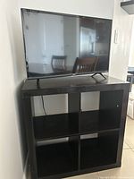 Dark brown wood TV stand with TV on top, showing four open square compartments.
