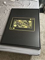 Top view of the framed King of Spades art print lying on a bed, showing the black background with gold card design.