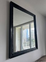 Full view of the large rectangular wall mirror mounted on wall showing the black wood frame and reflective glass surface.