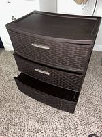 Brown plastic storage drawer unit with three pull-out drawers, two drawers open showing interior, woven texture design on drawer fronts.