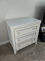 Front view of the white wicker dresser showing three drawers, round wicker knobs, and woven wicker construction.