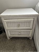 Front view of white wicker coastal nightstand showing drawer fronts and wicker texture.