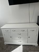 Front view of white wooden dresser showing drawers and side cabinets with metal handles and knobs.