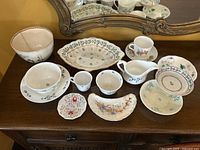 Overview photo displaying all china pieces arranged on a wooden surface in front of a mirror, showing the variety of floral china dishes and serving pieces.