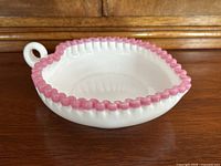 Side angle view of the heart-shaped milk glass dish showing the pink ruffled edge and rounded handle.