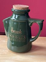 Front view of green pottery Harrods peanut pourer with cork top showing gold details and spouted design