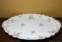 Front view of ornate, scalloped edge Limoges platter with pink floral patterns and gold trim on handles and edges.