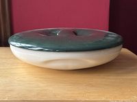 Side view showing the shallow white divided dish and rounded green lid with integrated handle grip.