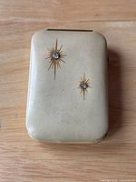 Front view of vintage beige leather wrapped key case with two starburst designs with embedded gems.