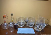 Overview of assorted mid-century glassware collection including decanters, bowls, martini glass, water pitcher, candleholder, paperweight, and tray