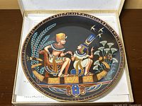 Porcelain plate in original box, showing Egyptian figures on a boat with detailed decorations and hieroglyphic border.